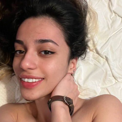 A young woman featured on free OnlyFans smiles softly while lying on a bed, her relaxed expression and minimalistic style creating a natural and intimate atmosphere.